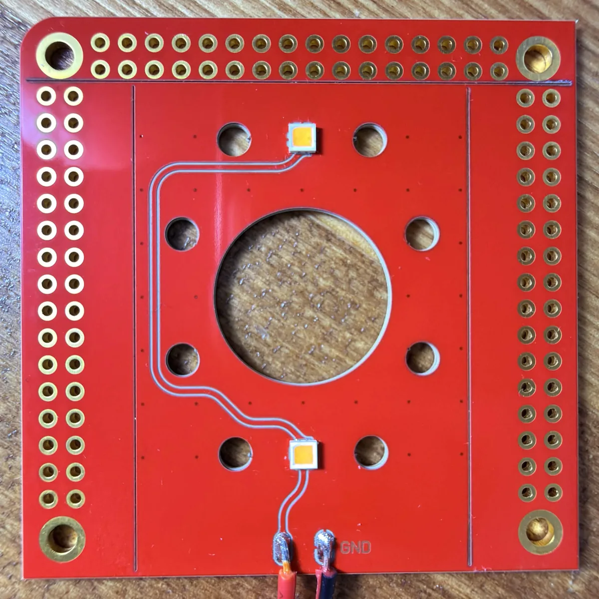 A PewCB LED board in one piece, with laser-cut round cutouts and V-score lines separating the edge strips